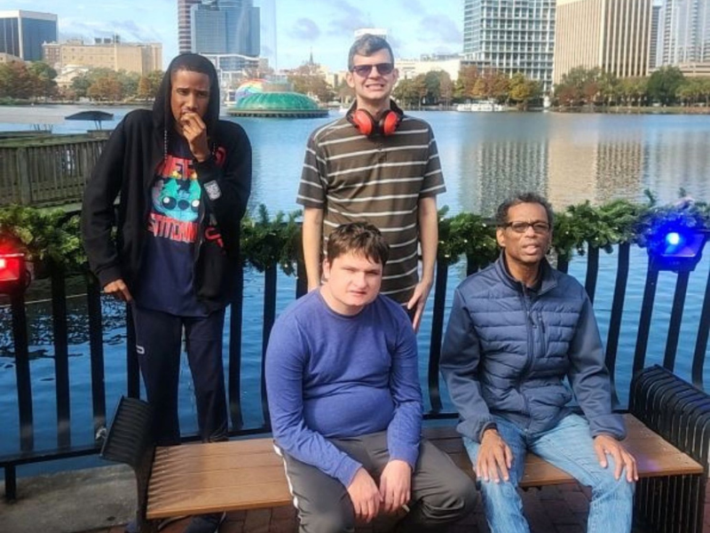 Four adults pose next to each other in front of a large lake with a fountain at the center.