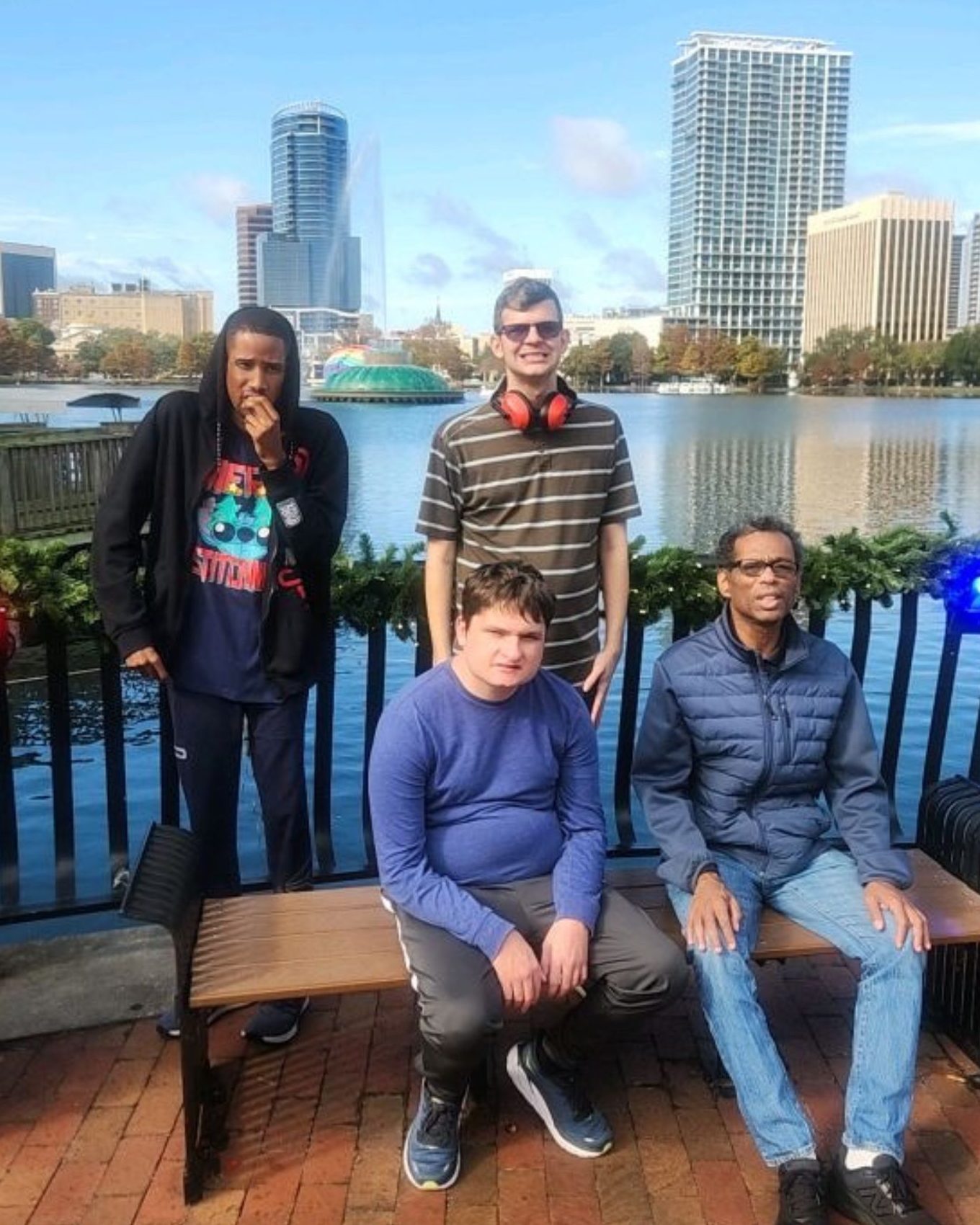 Four individuals pose by the water at Lake Eola with city buildings and a fountain in the background.