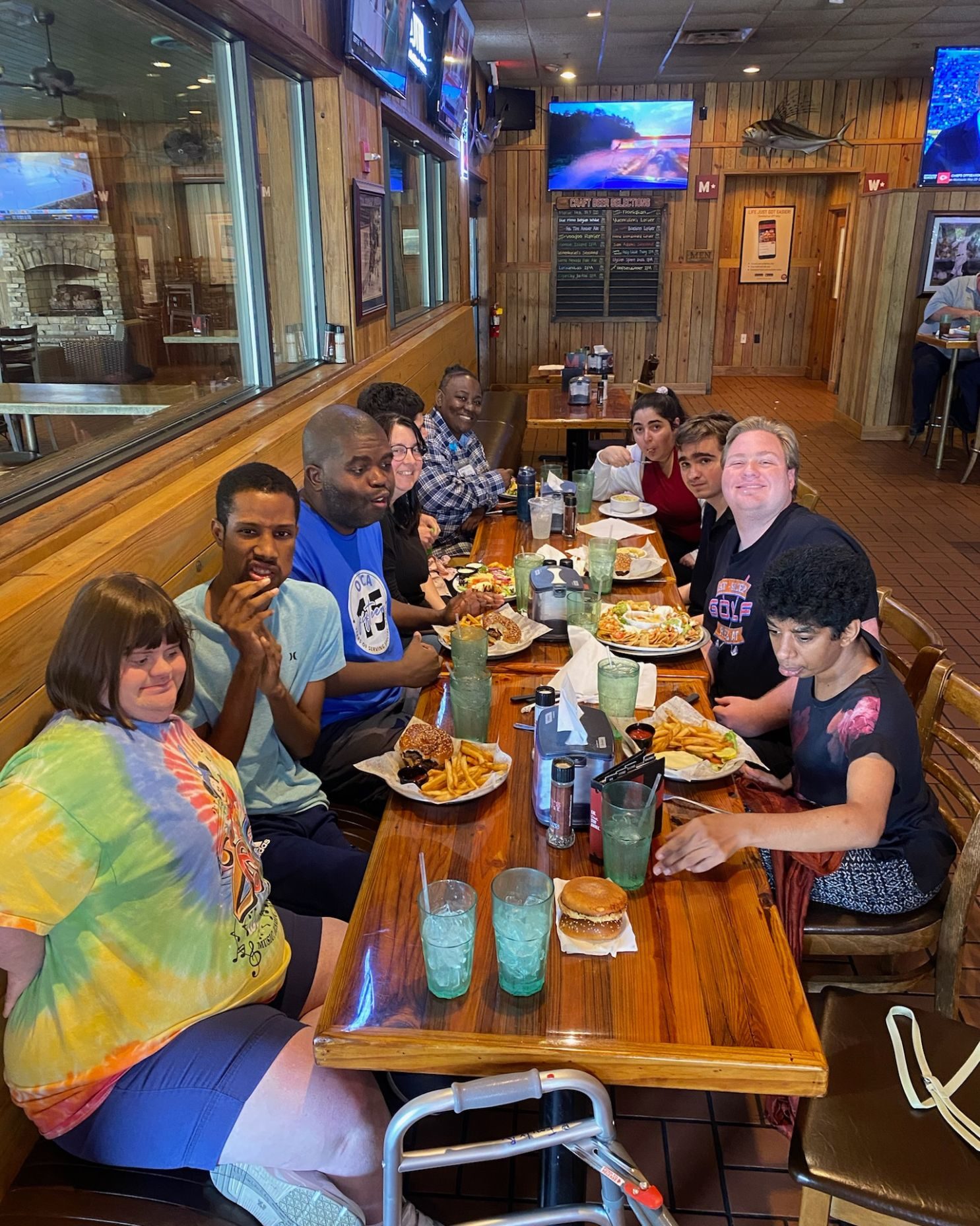 A group of friends gathers around a long table at a restaurant, enjoying burgers, fries, and laughter.