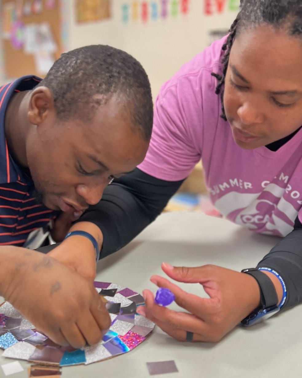 A participant and staff member work together on a mosaic art project using shiny square tiles.