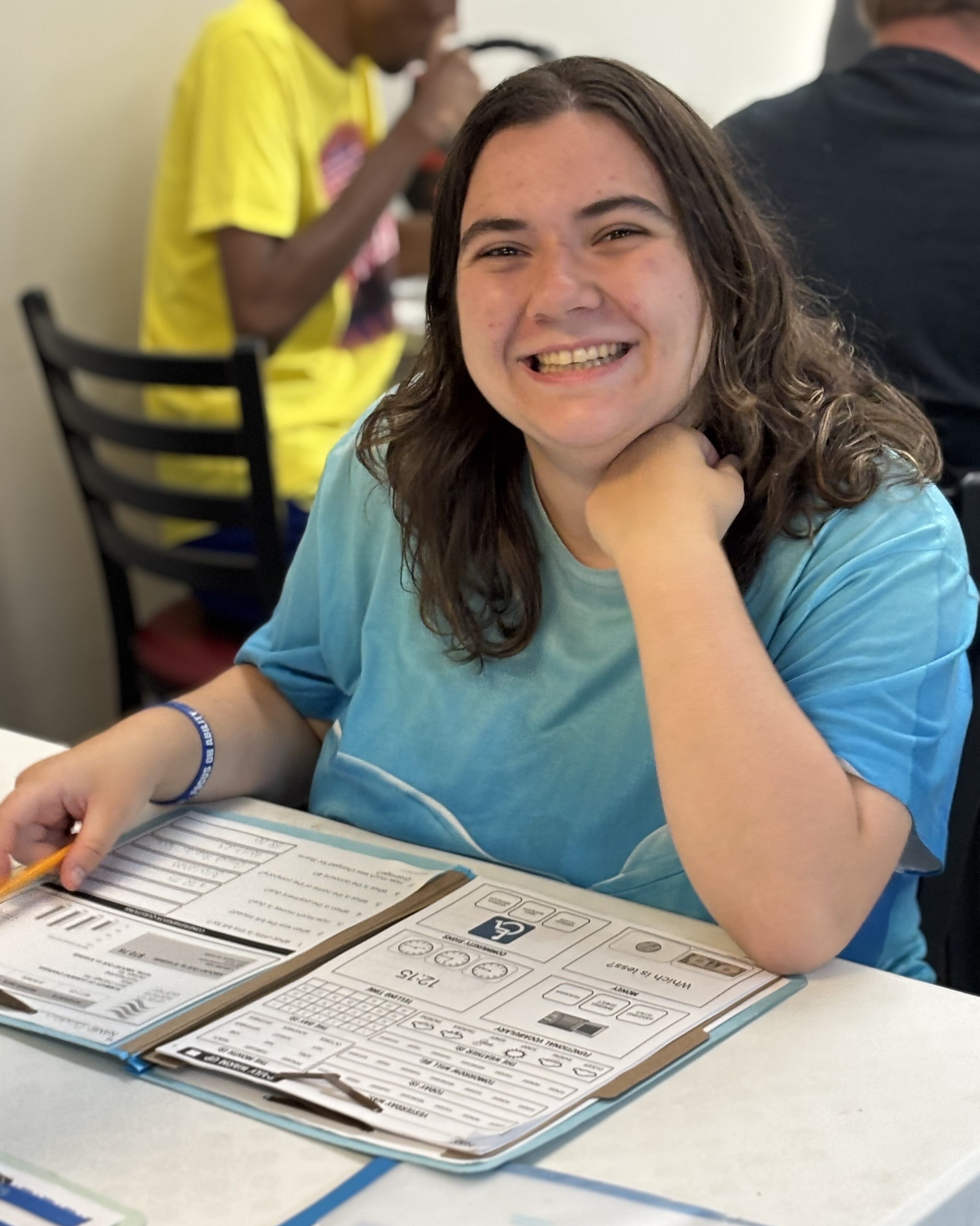 A young woman sits at a table with a worksheet in front of her. She is smiling for the camera.