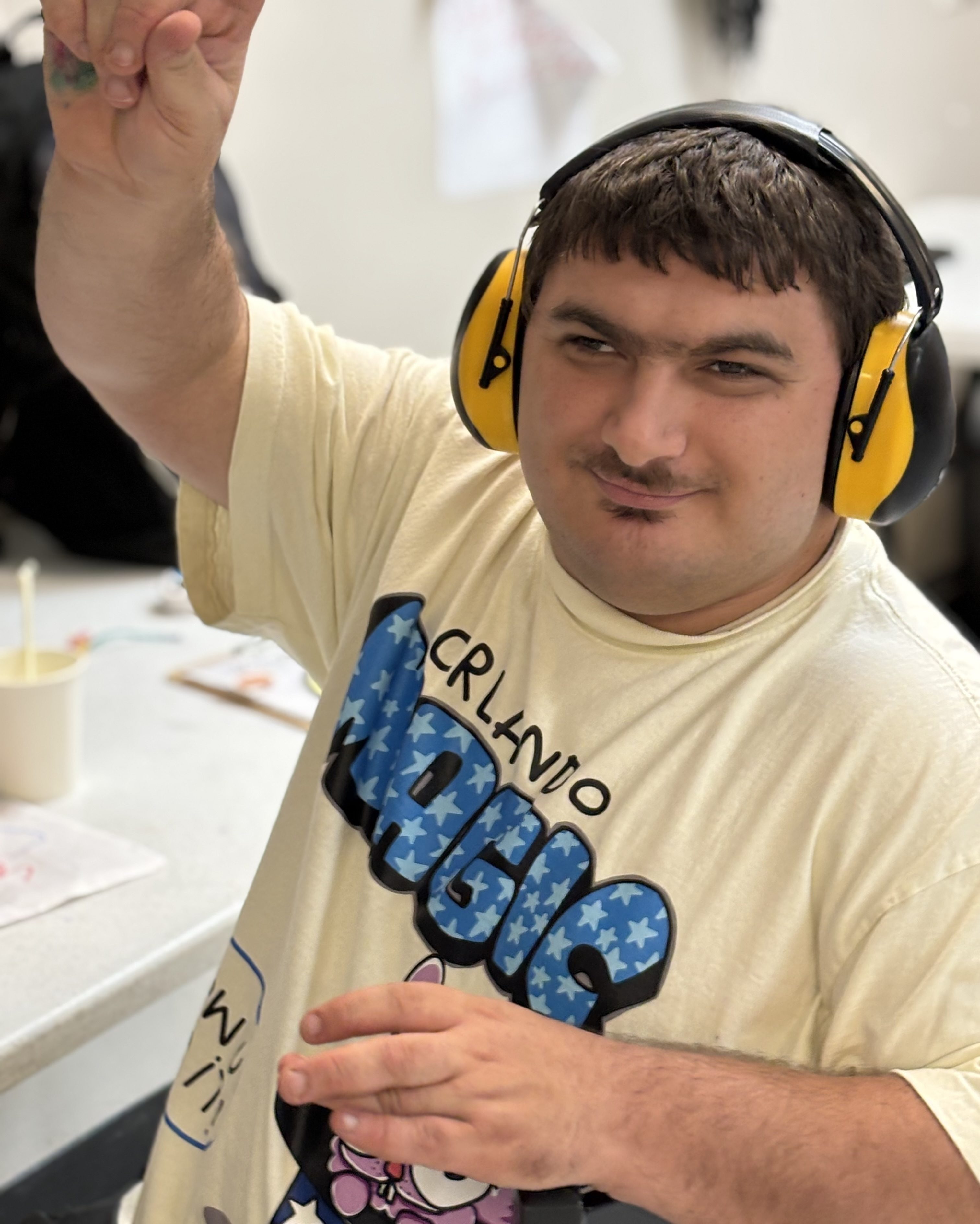 A man wearing sound cancelling headphones smiles at the camera. He has a mustache and is sitting at a table.