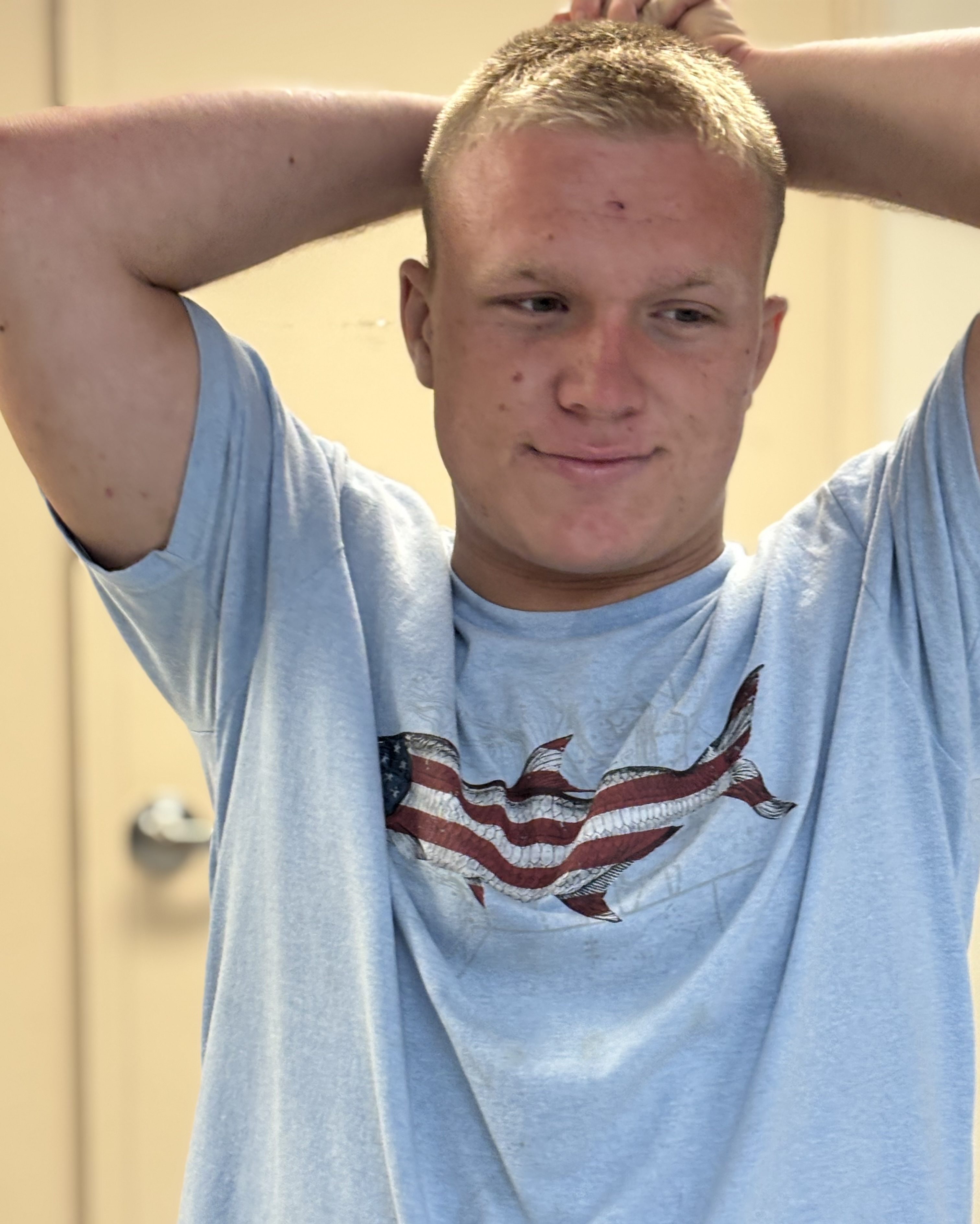 A man with short hear smiles at the camera. He is wearing a shirt with a fish on it.